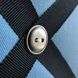 Close-up of navy ribbon and antique nickel button details on blue cotton fabric